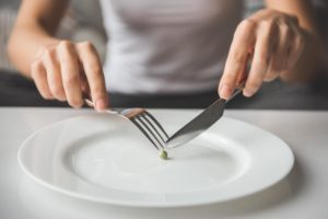 someone uses a knife and fork to try and cut a single pea in half for a meal