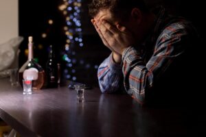 a person sits in front of a bottle with their hands on their face wondering what is a functioning alcoholic